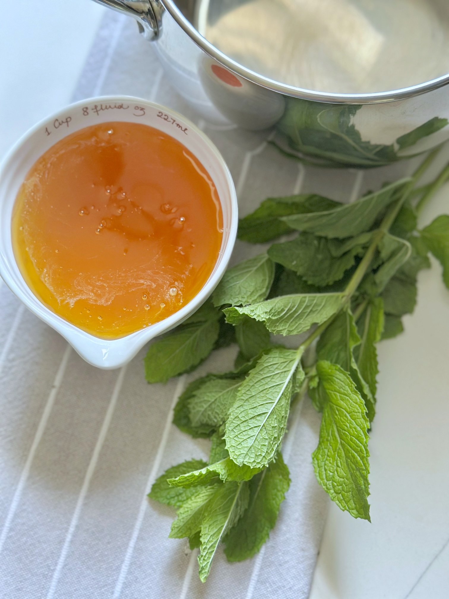 Honey in a measuring cup with fresh spearmint.