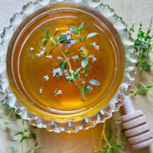 Top view of honey in a clear glass jar with leaves and flowers floating.